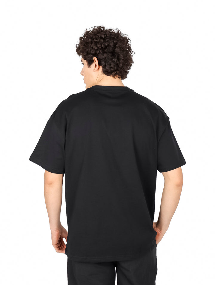 Hombre vistiendo playera negra de manga corta con estampado gráfico en color ocre y blanco en el pecho.