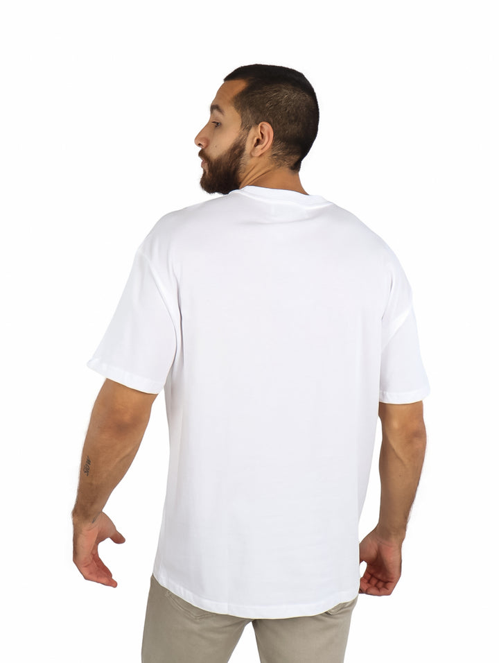 Hombre vistiendo playera blanca de manga corta con un detalle de bolsillo estampado multicolor en el pecho.