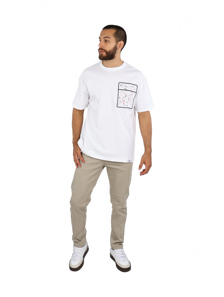 Hombre vistiendo playera blanca de manga corta con un detalle de bolsillo estampado multicolor en el pecho.