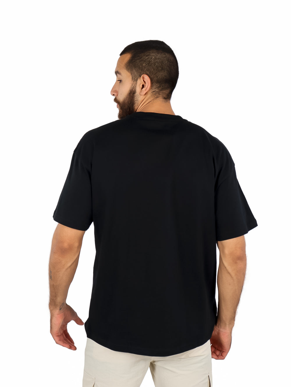 Hombre vistiendo playera negra de manga corta con un detalle decorativo cuadrado en el pecho izquierdo.