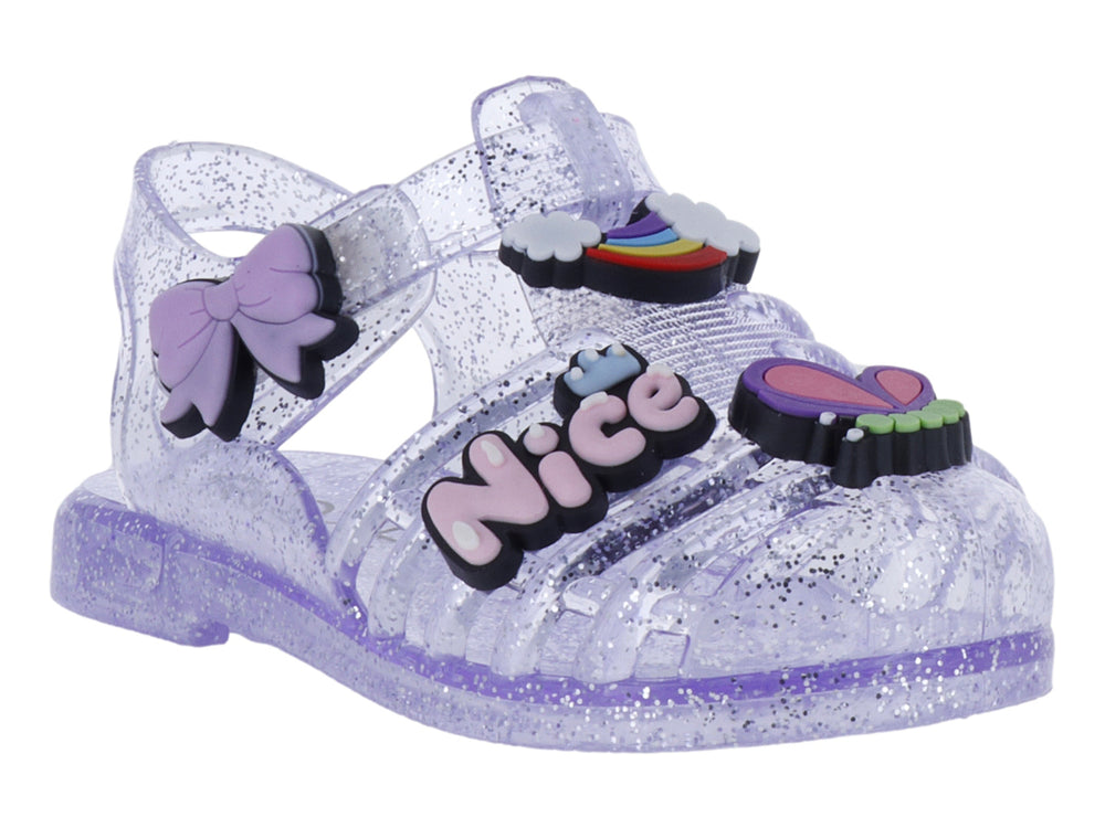Sandalias infantiles color morado con glitter, decoradas con un moño y letras que dicen 'Nice'.