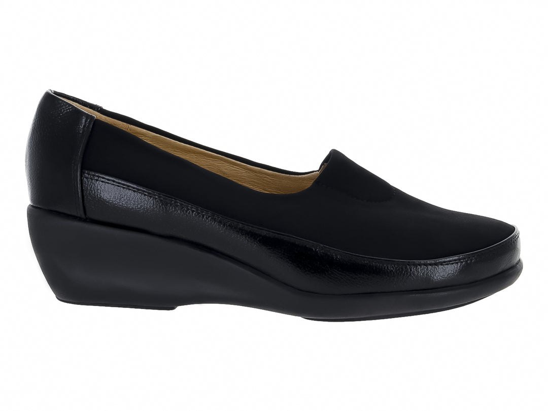 Zapato negro cerrado tipo slip-on con suela de cuña y materiales sintéticos y textiles.