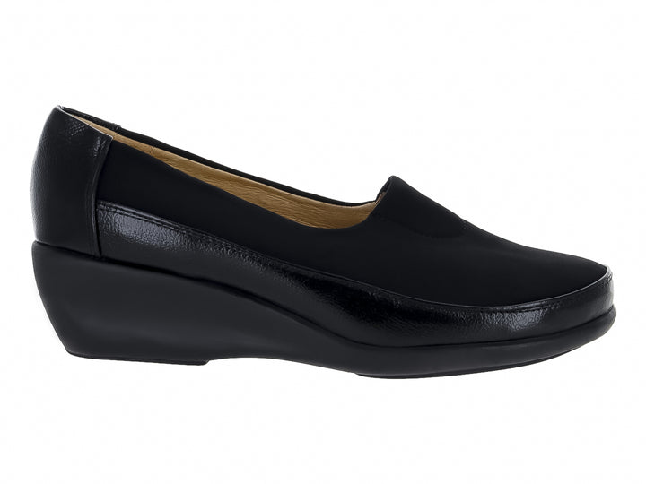 Zapato negro cerrado tipo slip-on con suela de cuña y materiales sintéticos y textiles.