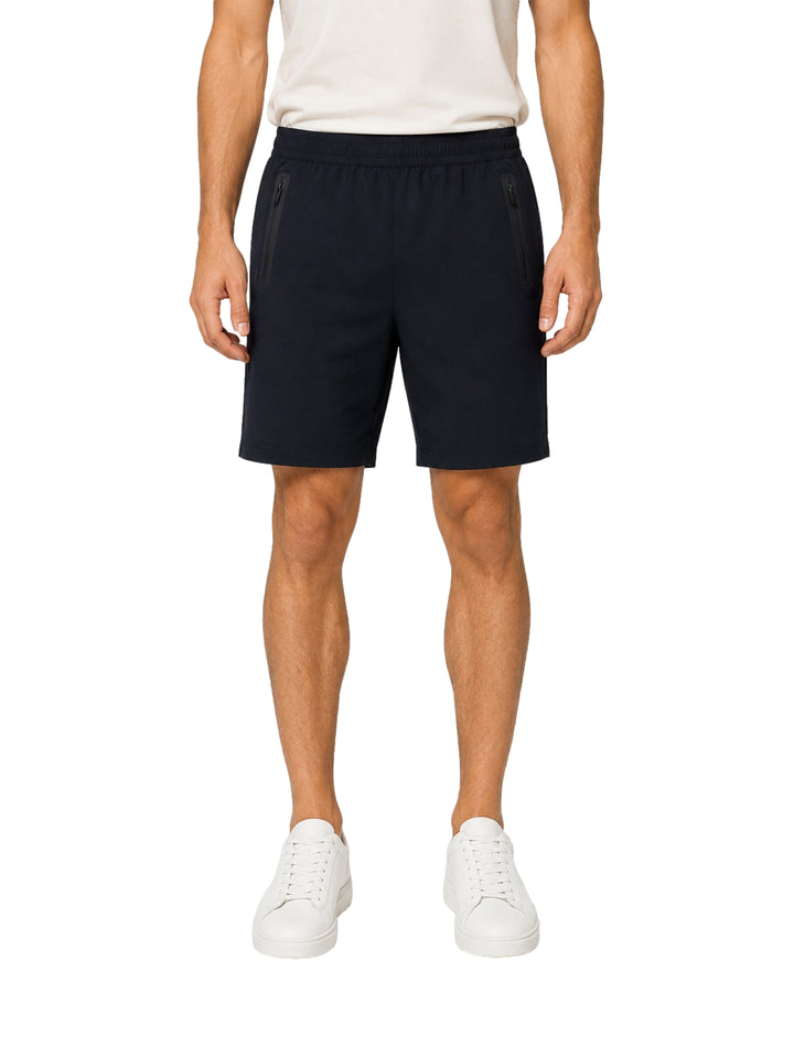 Hombre vistiendo shorts de surf color azul marino con cierres laterales y tenis blancos.