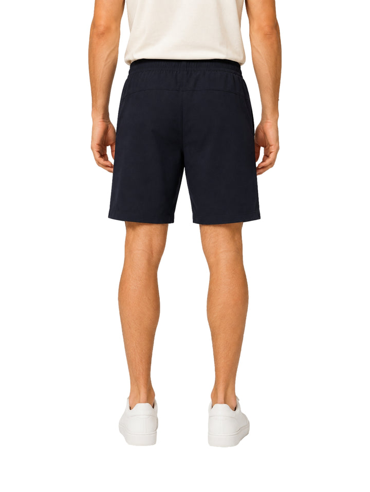 Hombre vistiendo shorts de surf color azul marino con cierres laterales y tenis blancos.