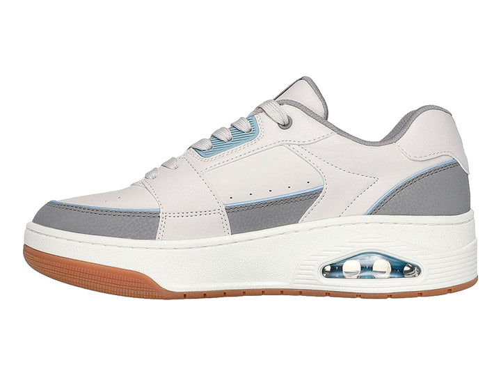 Tenis Skechers One Court color beige y gris con suela marrón y cámara de aire en el talón.