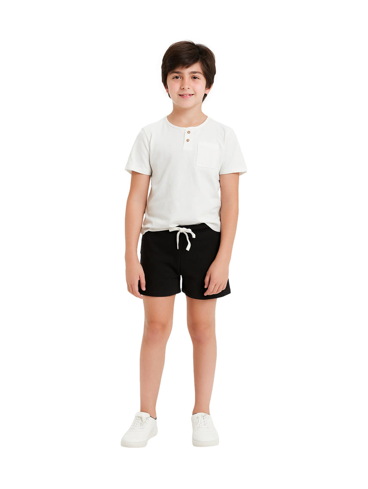 Niño vistiendo un conjunto de camiseta blanca y short negro con tenis blancos.