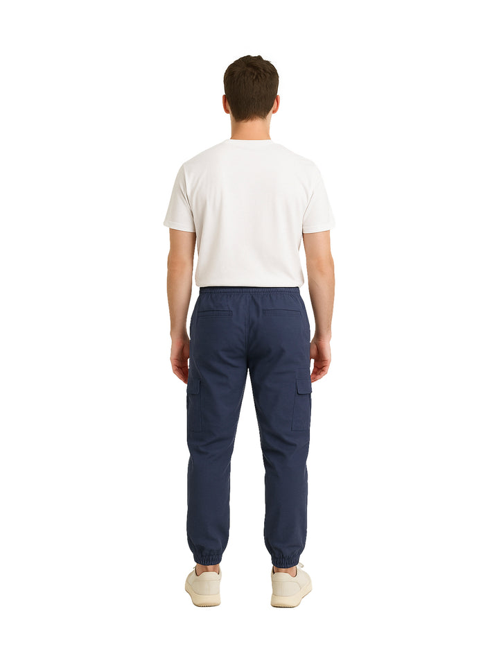 Hombre vistiendo pantalón jogger cargo color azul marino con camiseta blanca y tenis beige.