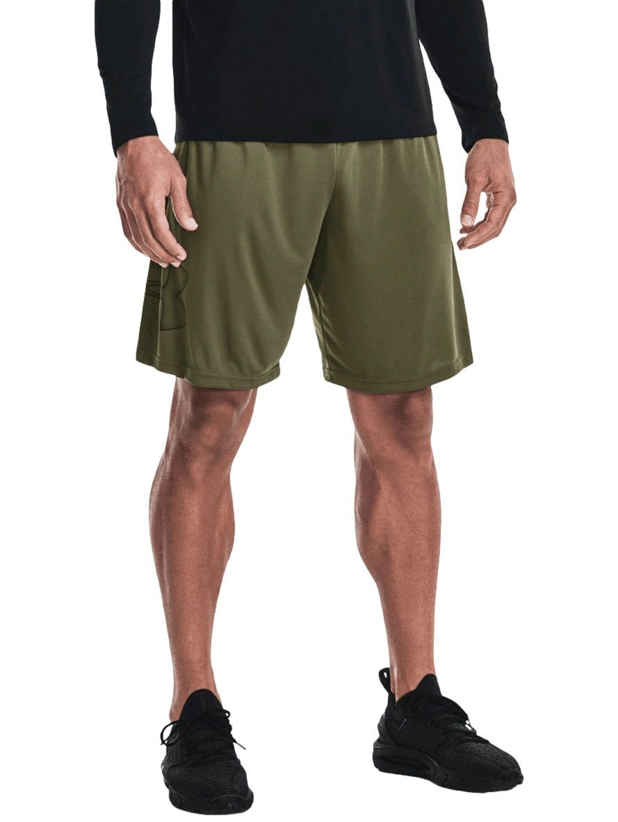 Hombre vistiendo shorts deportivos Under Armour color verde oliva con camiseta negra y tenis negros.