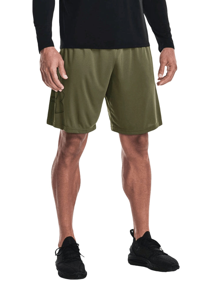 Hombre vistiendo shorts deportivos Under Armour color verde oliva con camiseta negra y tenis negros.
