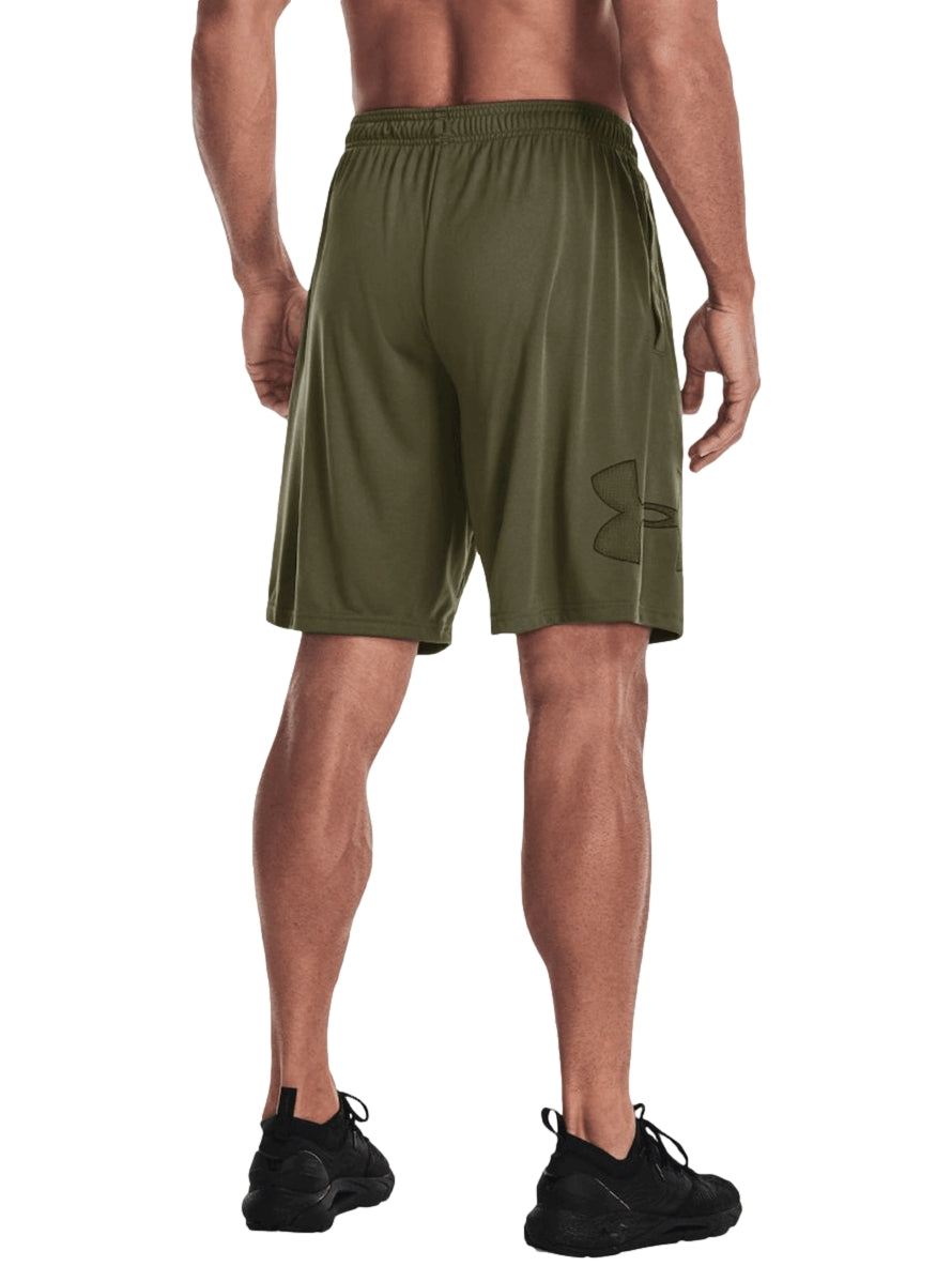Hombre vistiendo shorts deportivos Under Armour color verde oliva con camiseta negra y tenis negros.