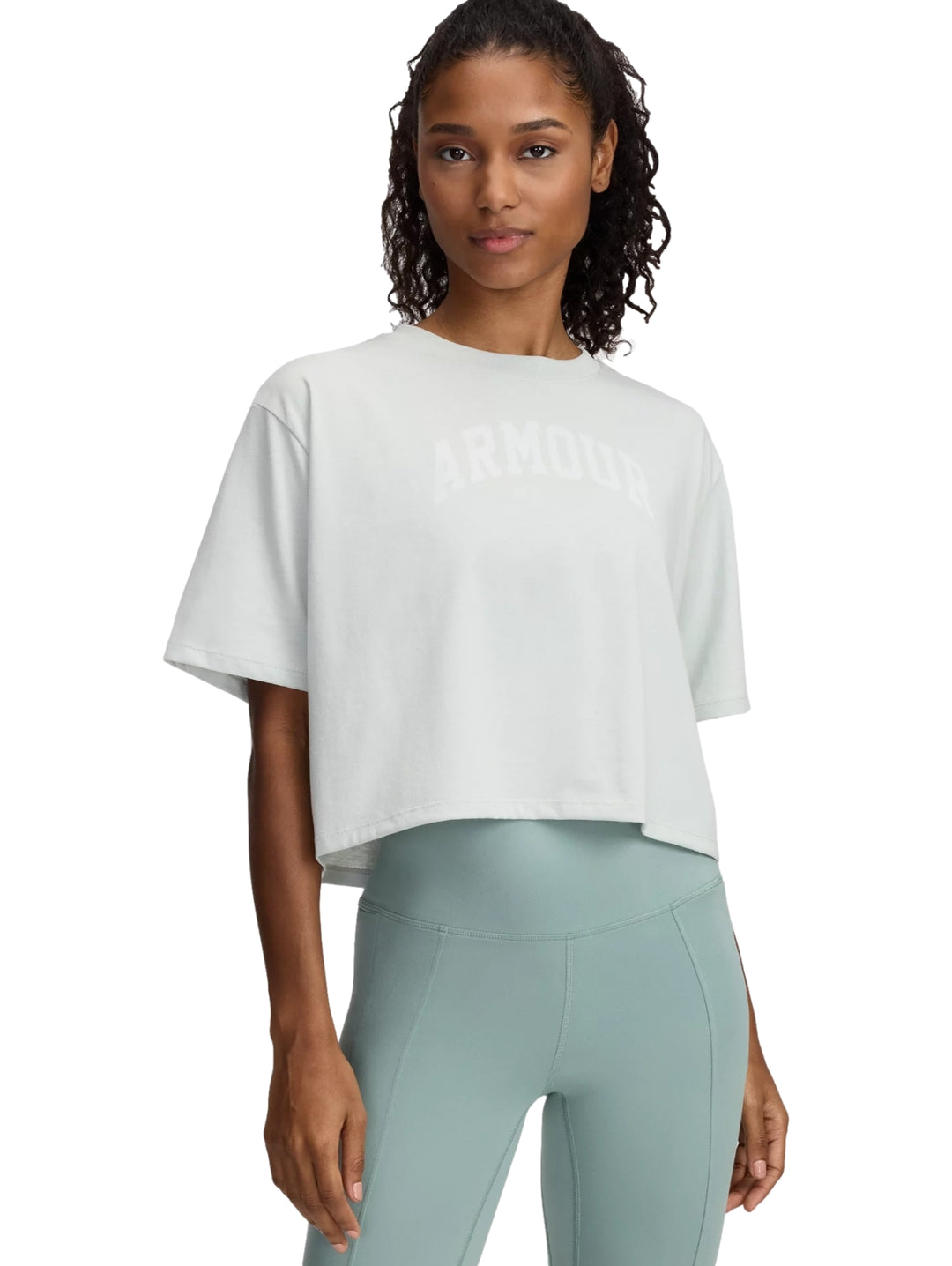 Mujer vistiendo playera Under Armour color verde hidro con leggings a juego.