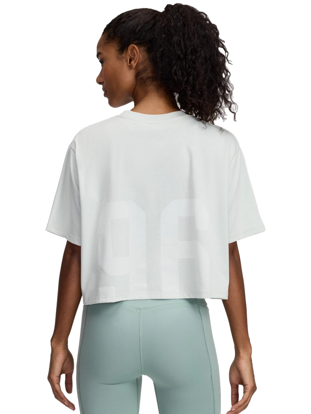 Mujer vistiendo playera Under Armour color verde hidro con leggings a juego.