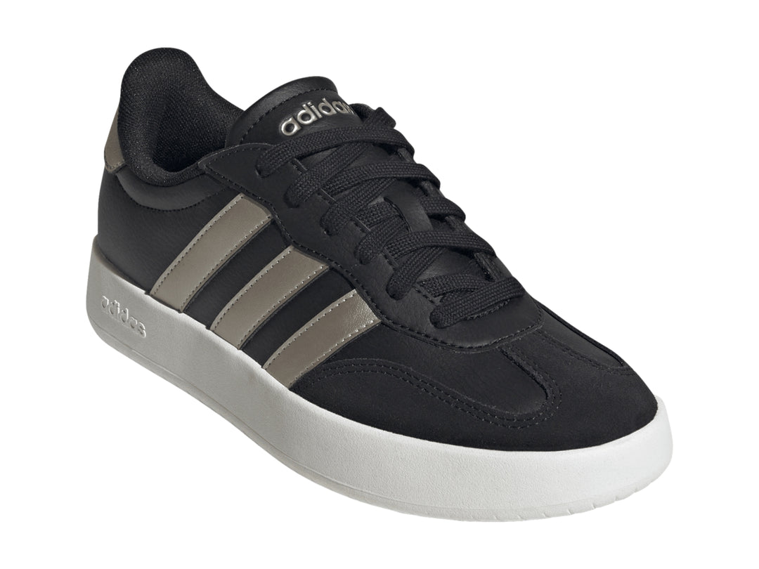 Tenis Adidas color negro con tres franjas doradas y suela blanca.