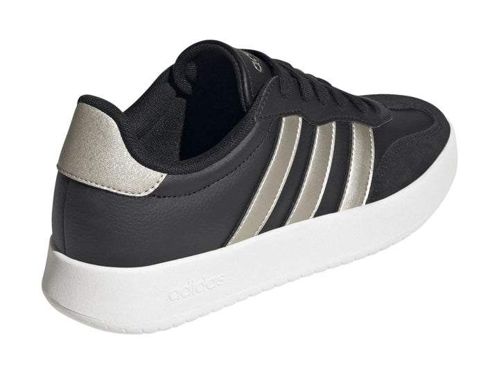 Tenis Adidas color negro con tres franjas doradas y suela blanca.