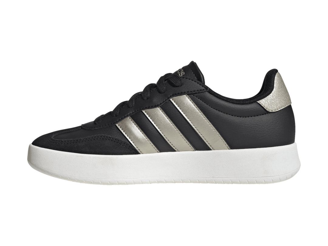 Tenis Adidas color negro con tres franjas doradas y suela blanca.