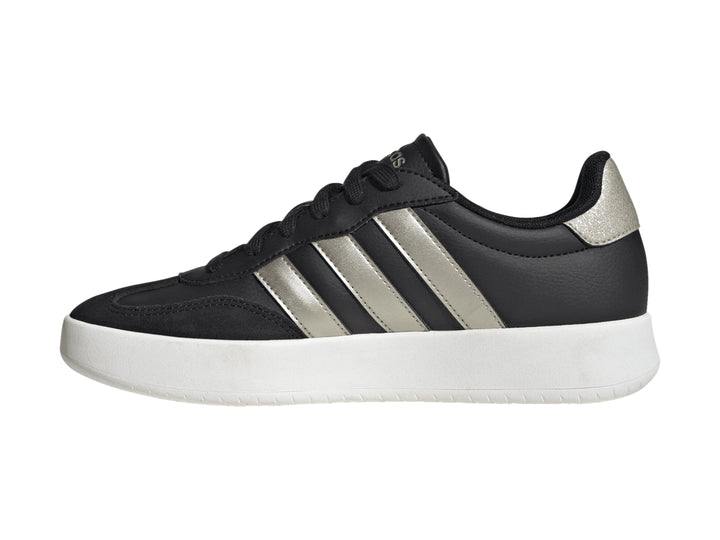 Tenis Adidas color negro con tres franjas doradas y suela blanca.