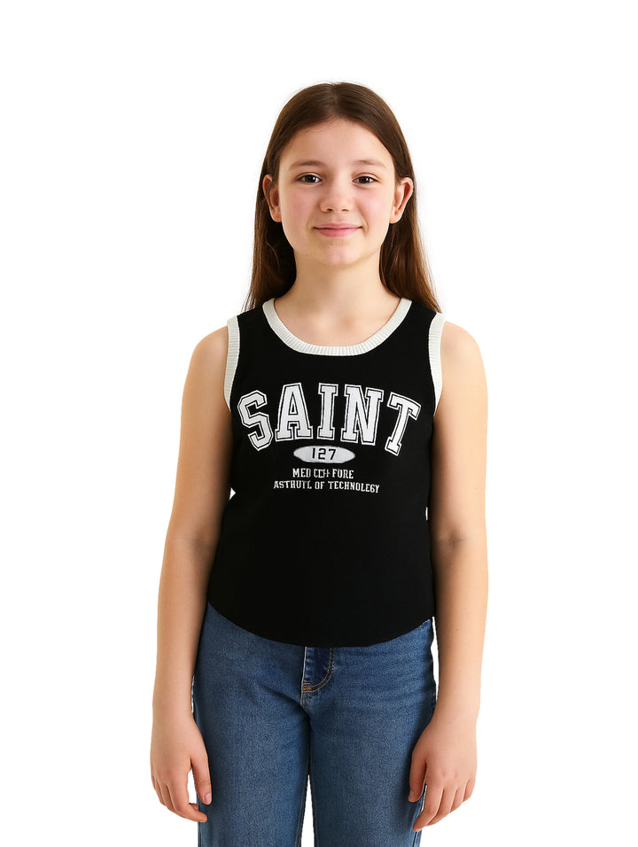 Niña vistiendo un top sin mangas color negro con rib blanco en el cuello y estampado frontal blanco que dice SAINT.
