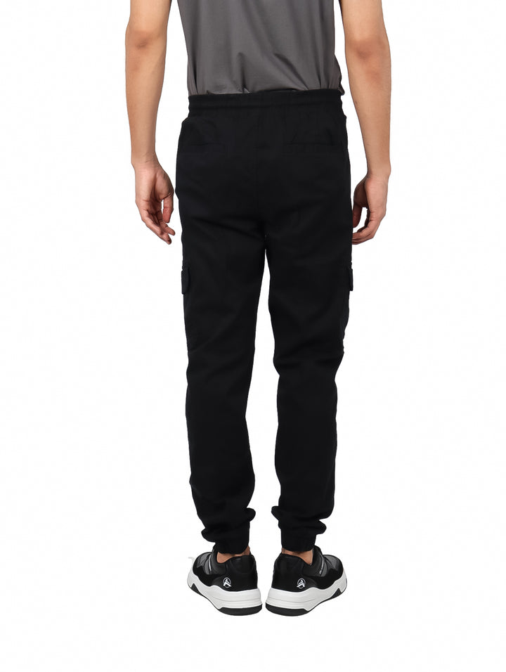 Hombre vistiendo pantalones jogger color negro con bolsillos laterales tipo cargo y puños ajustados.