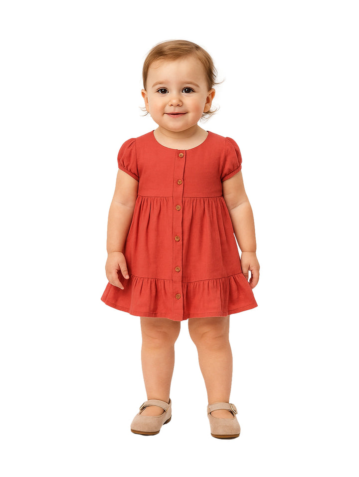 Niña pequeña vistiendo un vestido rojo de botones con manga corta y zapatos color beige.