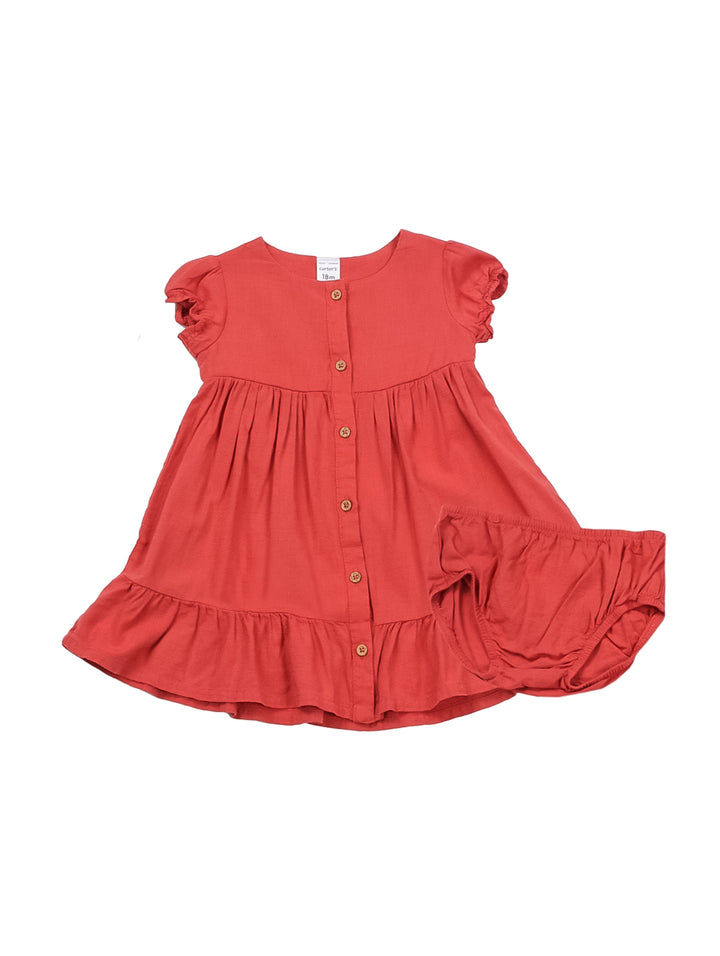 Niña pequeña vistiendo un vestido rojo de botones con manga corta y zapatos color beige.