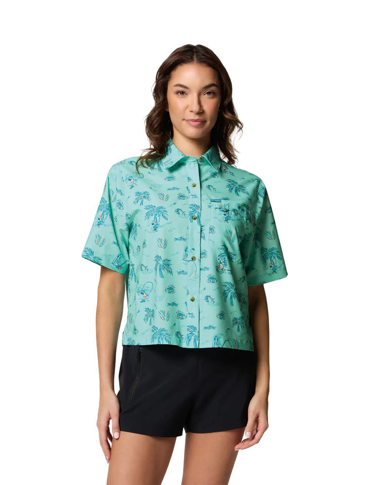Mujer vistiendo camisa Columbia color verde menta con estampado tropical de palmeras y shorts negros.
