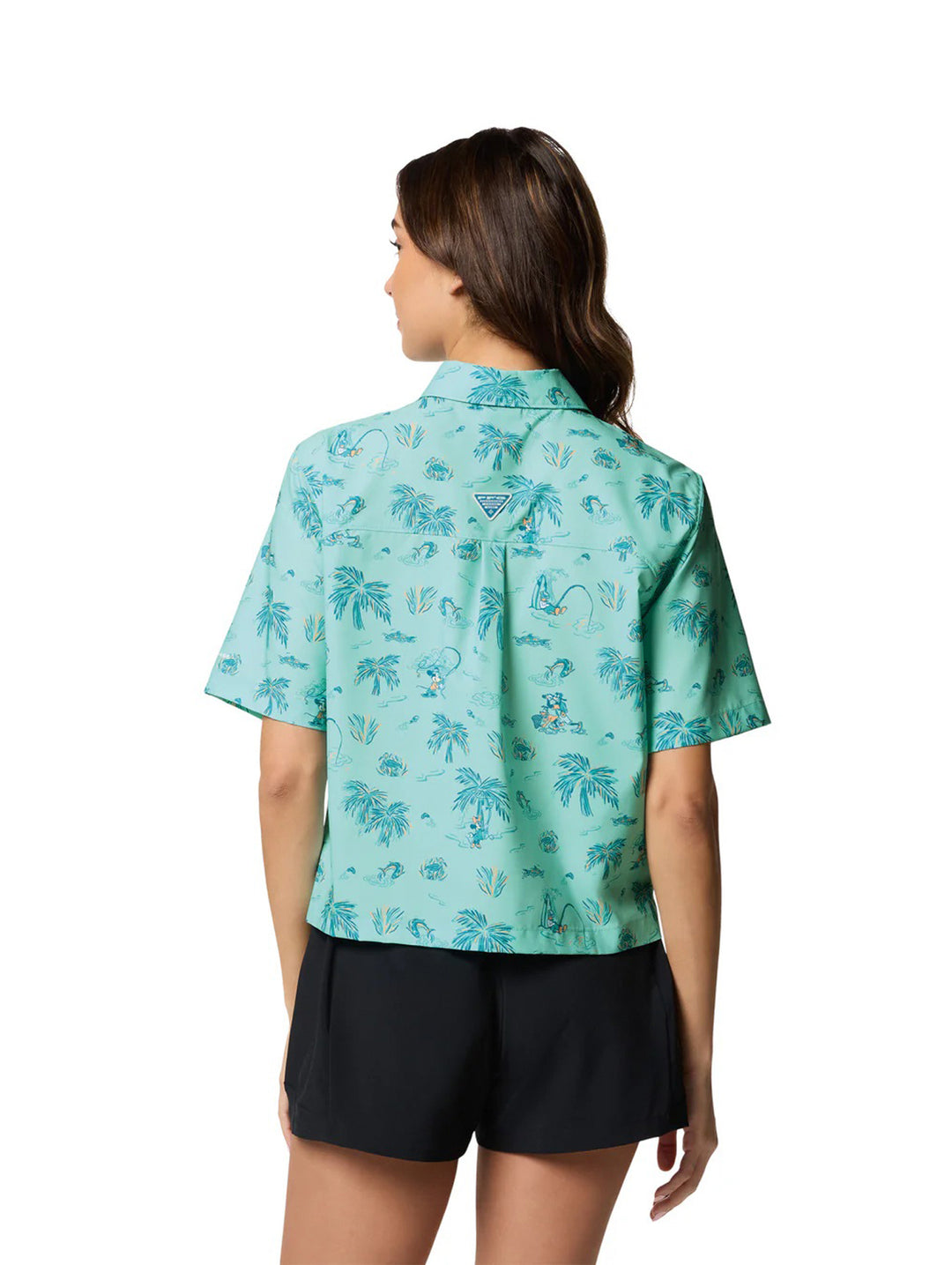 Mujer vistiendo camisa Columbia color verde menta con estampado tropical de palmeras y shorts negros.