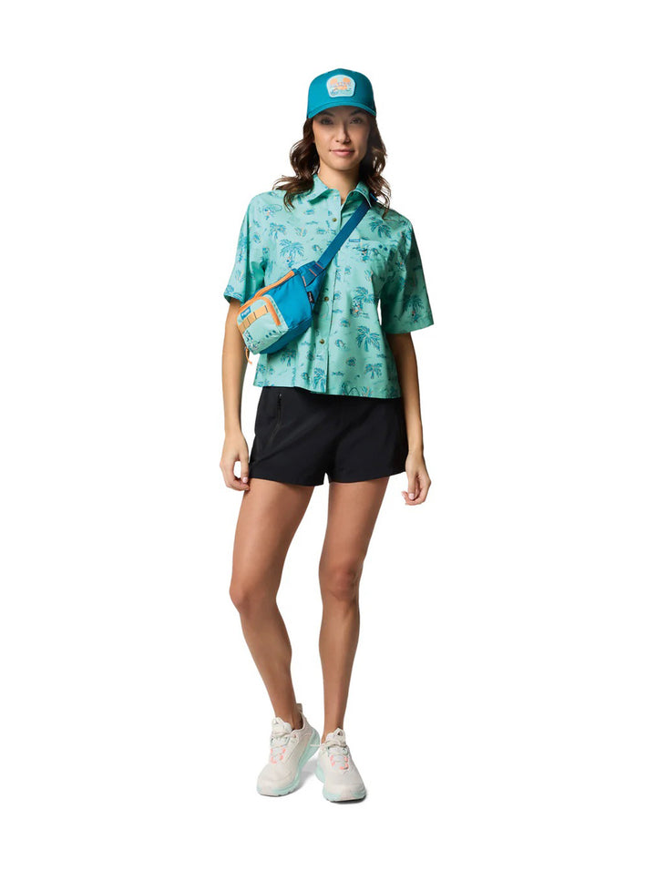 Mujer vistiendo camisa Columbia color verde menta con estampado tropical de palmeras y shorts negros.
