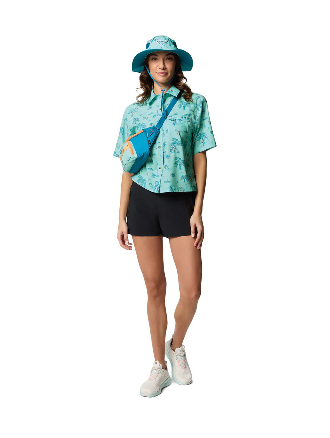 Mujer vistiendo camisa Columbia color verde menta con estampado tropical de palmeras y shorts negros.