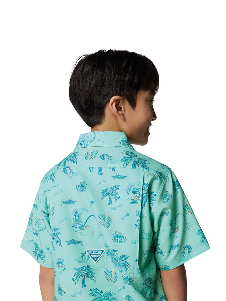 Niño vistiendo una camisa Columbia de manga corta color turquesa con estampado tropical de palmeras.