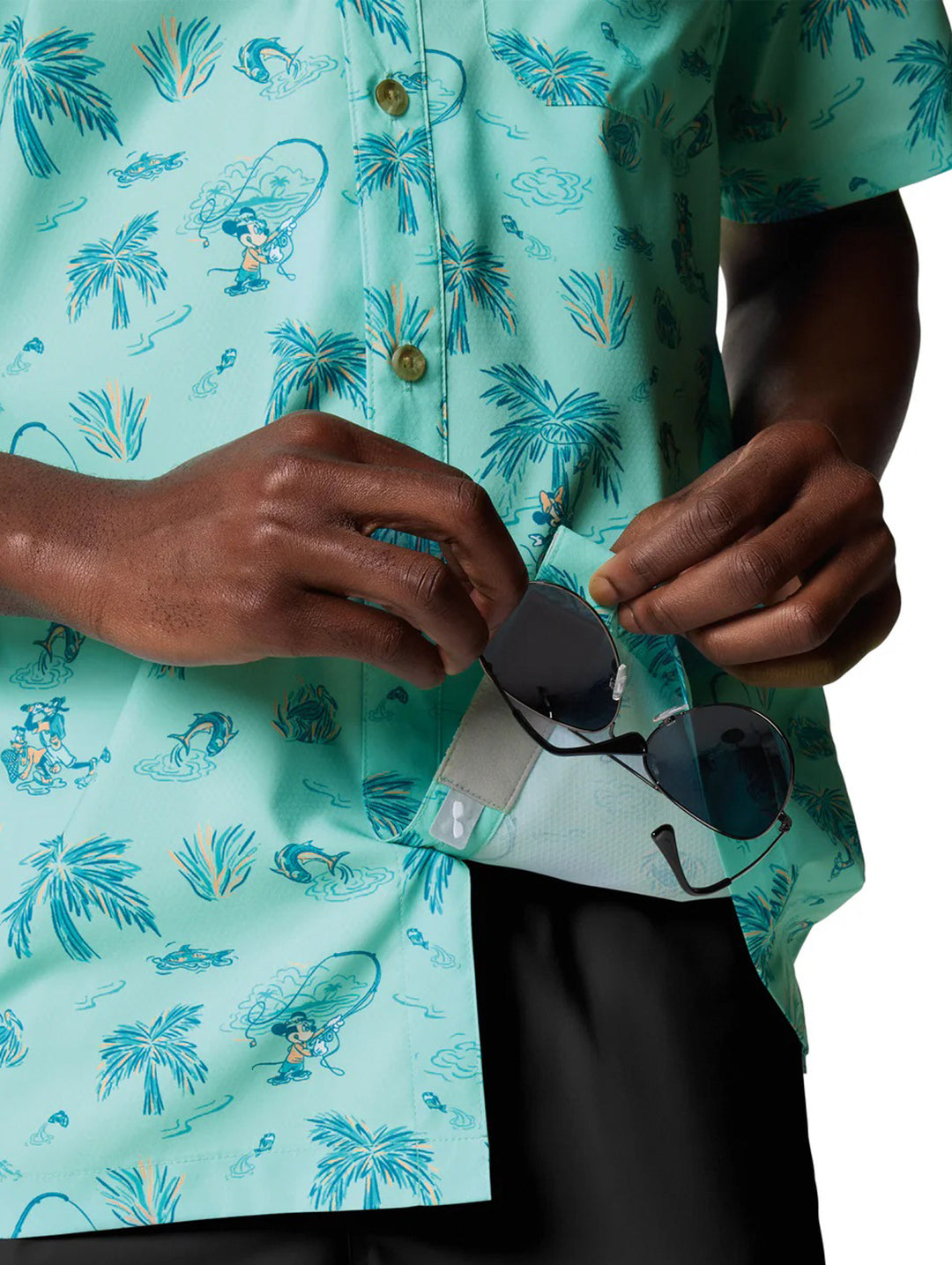 Hombre vistiendo camisa Columbia de manga corta color turquesa con estampado tropical de palmeras.