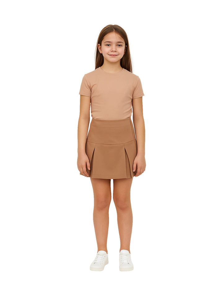 Niña vistiendo una falda plisada color café y camiseta a juego sobre fondo blanco.