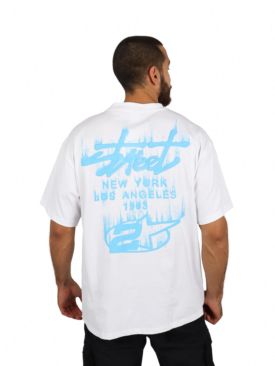 Hombre vistiendo una playera blanca oversize de manga corta con un logo en el pecho.