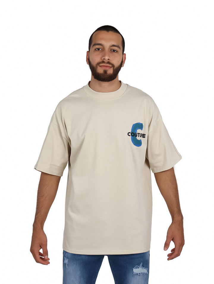 Hombre vistiendo playera beige de manga corta con diseño gráfico azul en el pecho.