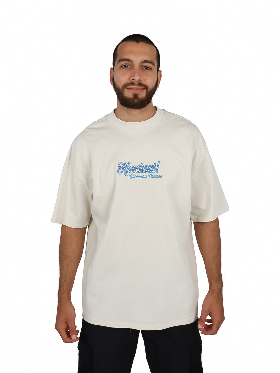 Hombre vistiendo playera oversize color beige con logotipo azul en el pecho.