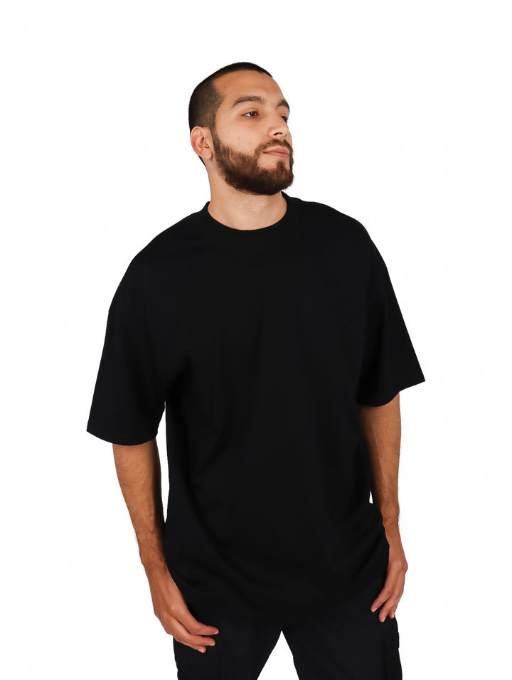 Hombre vistiendo una playera oversize de color negro con cuello redondo y manga corta sobre fondo blanco.