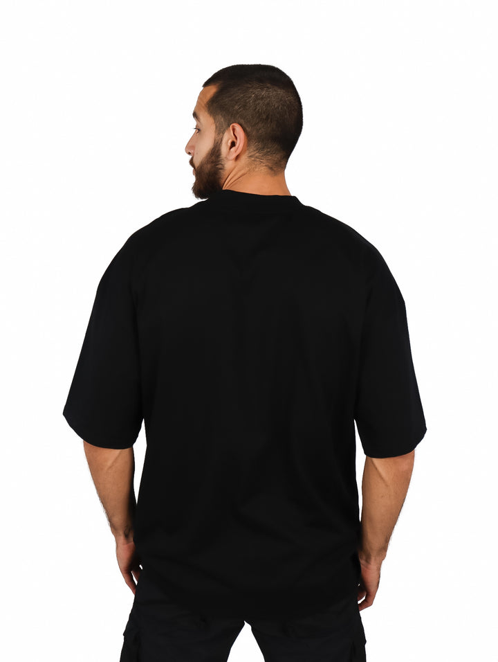 Hombre vistiendo una playera oversize de color negro con cuello redondo y manga corta sobre fondo blanco.