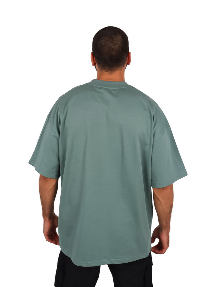Hombre vistiendo una playera oversize de color verde con cuello redondo y manga corta.