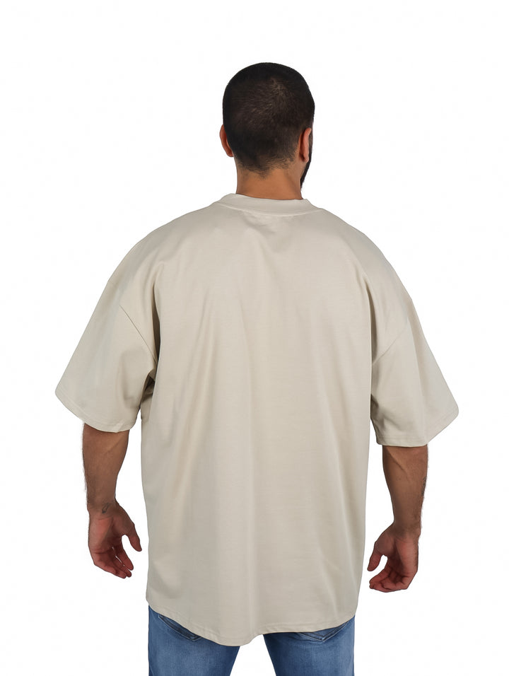 Hombre vistiendo una playera oversize de color khaki con cuello redondo y manga corta.