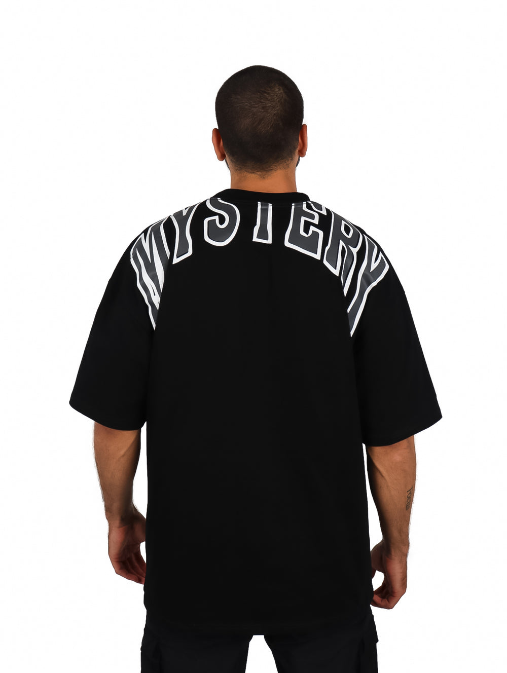 Hombre vistiendo una playera oversize de color negro con cuello redondo y manga corta.