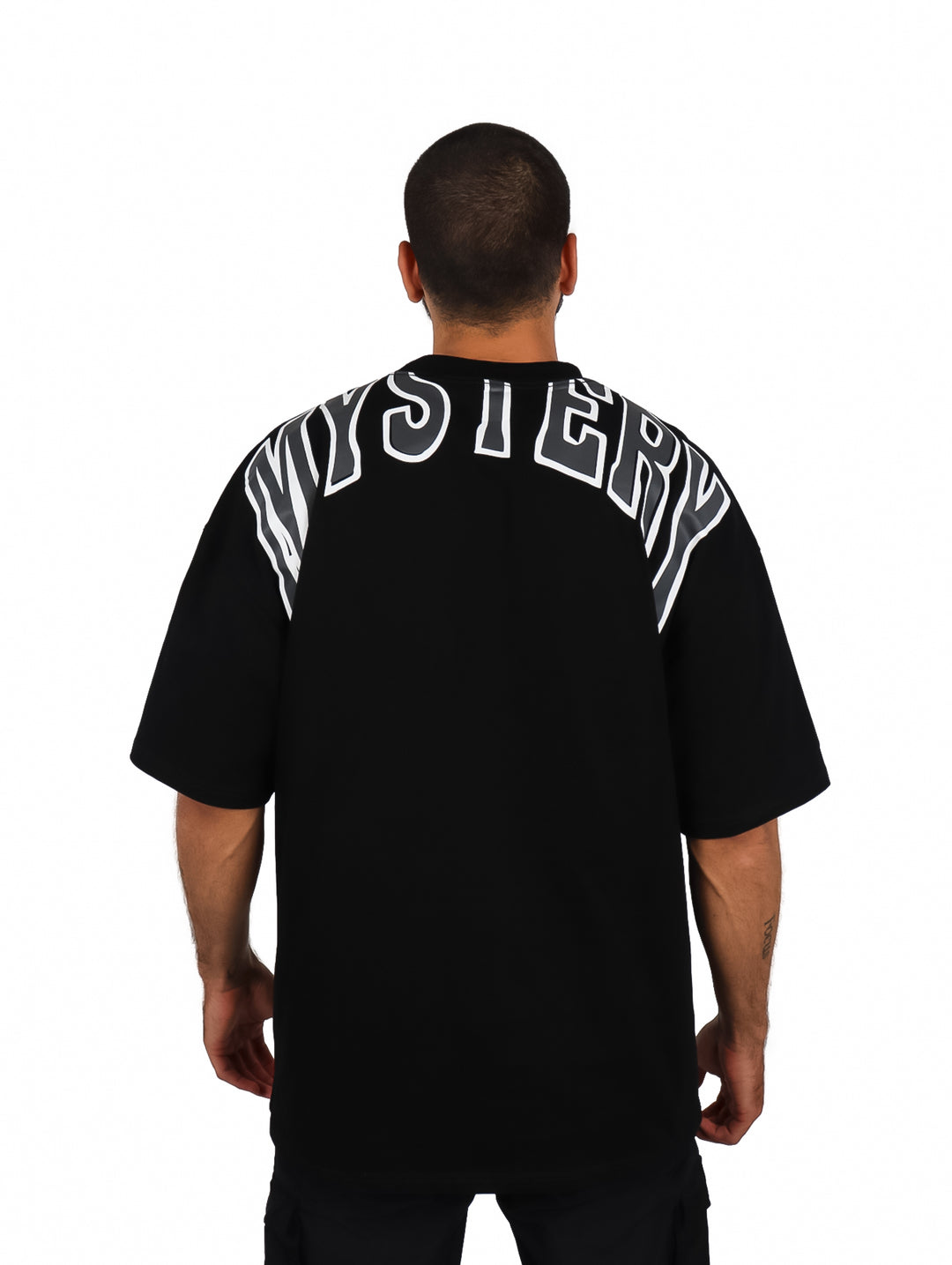 Hombre vistiendo una playera oversize de color negro con cuello redondo y manga corta.