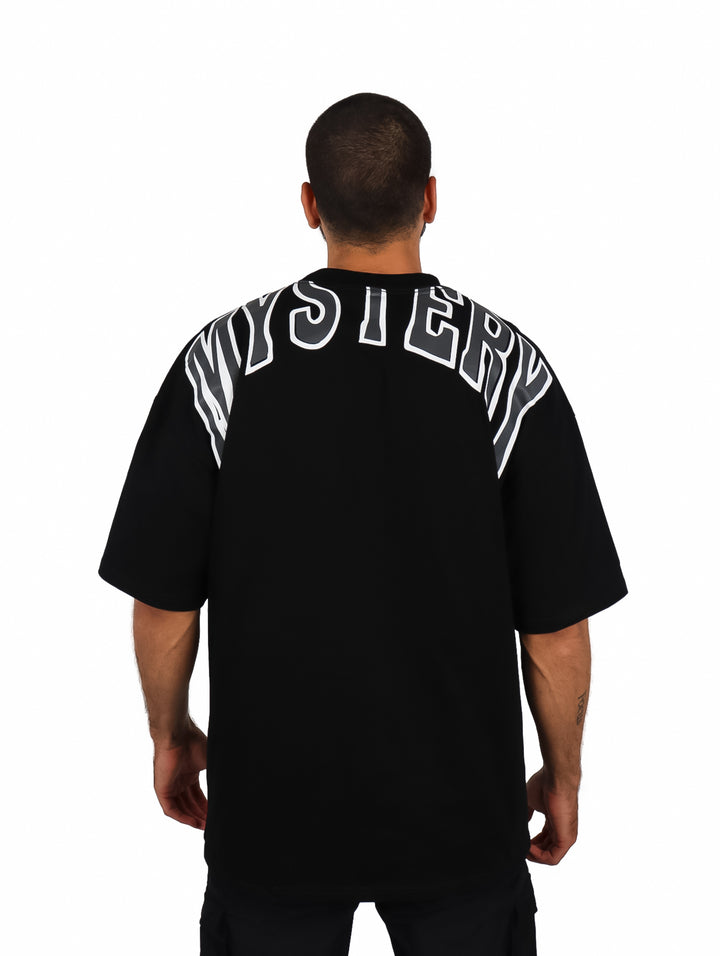Hombre vistiendo una playera oversize de color negro con cuello redondo y manga corta.