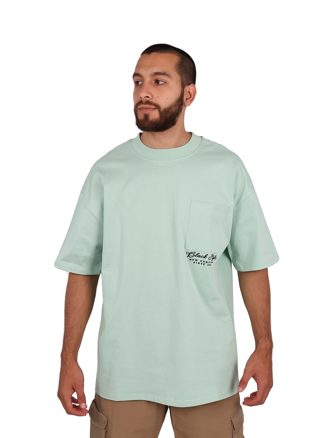 Hombre vistiendo playera oversize color menta con bolsillo frontal y cuello redondo.