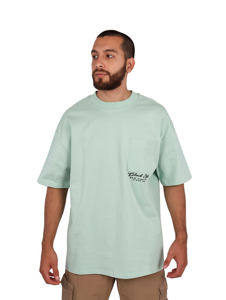 Hombre vistiendo playera oversize color menta con bolsillo frontal y cuello redondo.