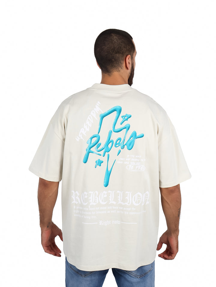 Hombre vistiendo playera oversize color arena con logo azul en el pecho.