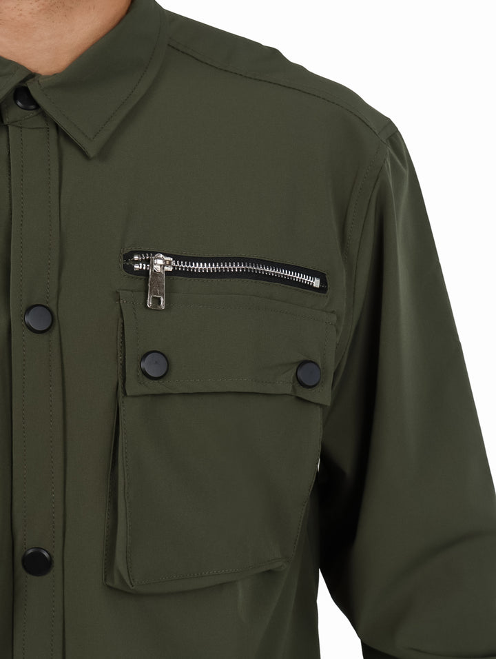 Hombre vistiendo camisa oversize color verde oliva con bolsillos frontales y manga larga.