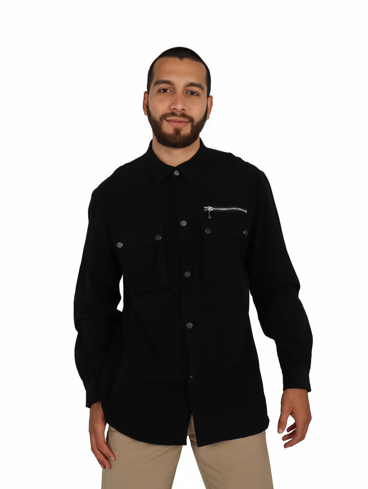Hombre vistiendo una camisa oversize color negro de manga larga con bolsillos frontales y cierre.