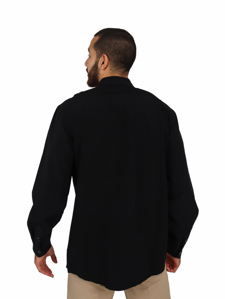 Hombre vistiendo una camisa oversize color negro de manga larga con bolsillos frontales y cierre.