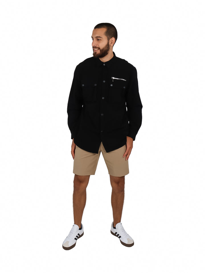 Hombre vistiendo una camisa oversize color negro de manga larga con bolsillos frontales y cierre.