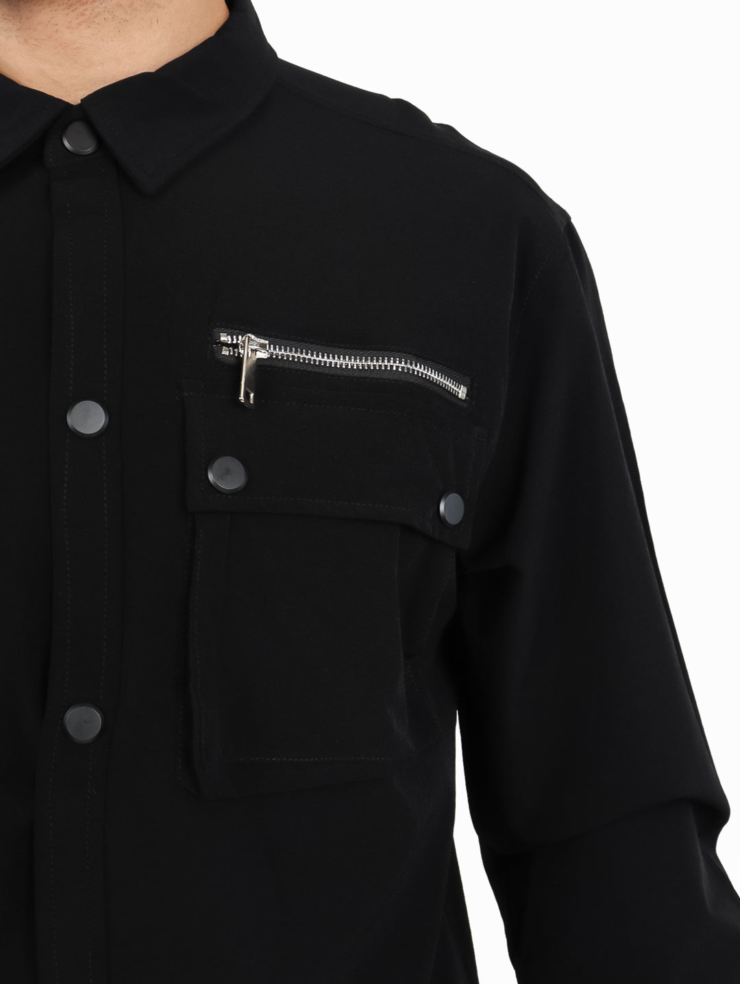 Hombre vistiendo una camisa oversize color negro de manga larga con bolsillos frontales y cierre.